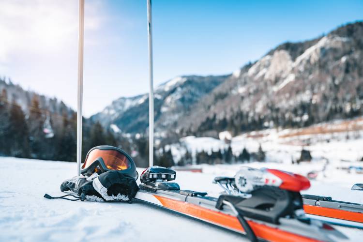 Close up of skis, ski goggles, ski gloves and ski poles. Sports equipment displayed in snow with magnificent mountains and clear sky in the background